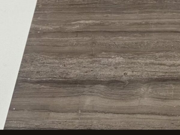 A cut sample of the dark coffee board: a warm deep brown with straight parallel darker veins running across it, photographed on a white bench.