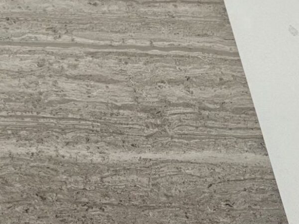 A cut sample of the dark grey board: a cool grey with stronger white veining running across it, photographed on a white bench.