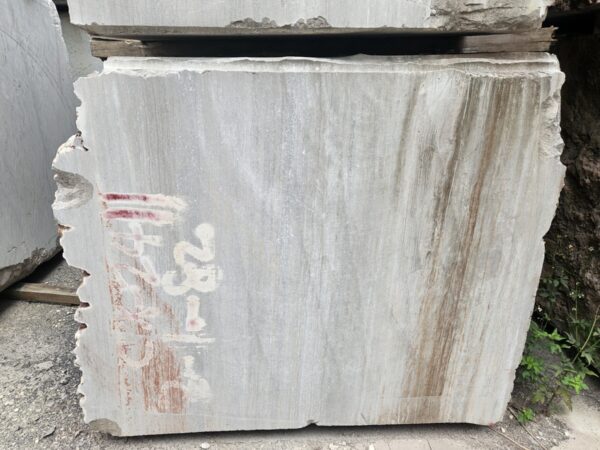 The sawn face of a block, pale grey with the straight parallel lines of the bed running down it, and the brown streaks where rainwater has carried iron out of the rock and down the face.