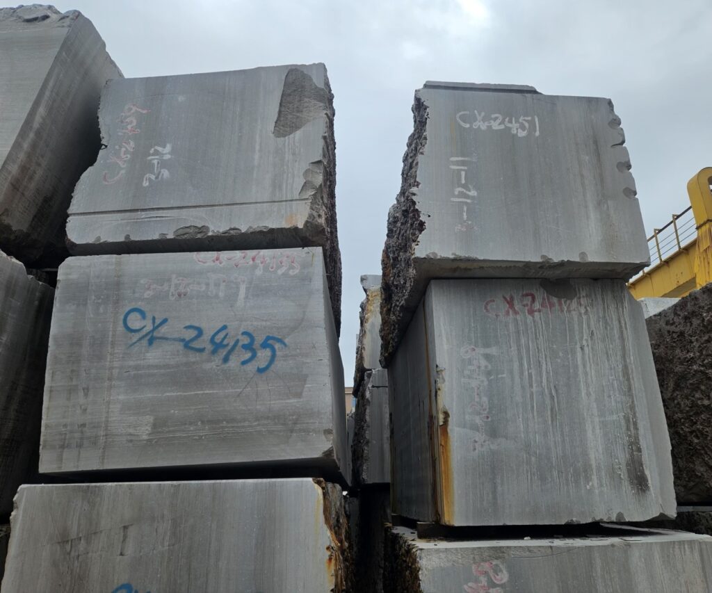 Blocks stacked in the yard with the quarry markings sprayed on them in red, the sawn face of the upper block showing the lines of the bed running the full height of it.