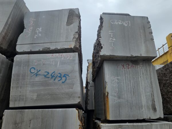 Blocks stacked in the yard with the quarry markings sprayed on them in red, the sawn face of the upper block showing the lines of the bed running the full height of it.