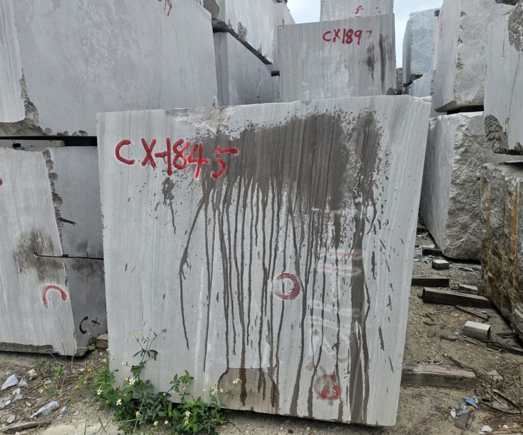 A block of this stone standing in the yard with the quarry marking CX-1845 sprayed on its sawn face in red, the straight lines of the bed running down it and the dark streaks of iron staining carried down the face by rainwater.