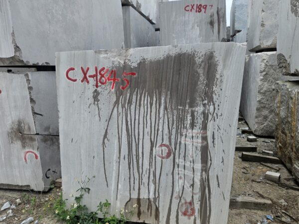 A block of this stone standing in the yard with the quarry marking CX-1845 sprayed on its sawn face in red, the straight lines of the bed running down it and the dark streaks of iron staining carried down the face by rainwater.