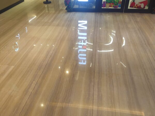 The floor of a shopping centre concourse laid in this stone, with a lit shop sign and a planter beside it and the sign reflected in the polish.