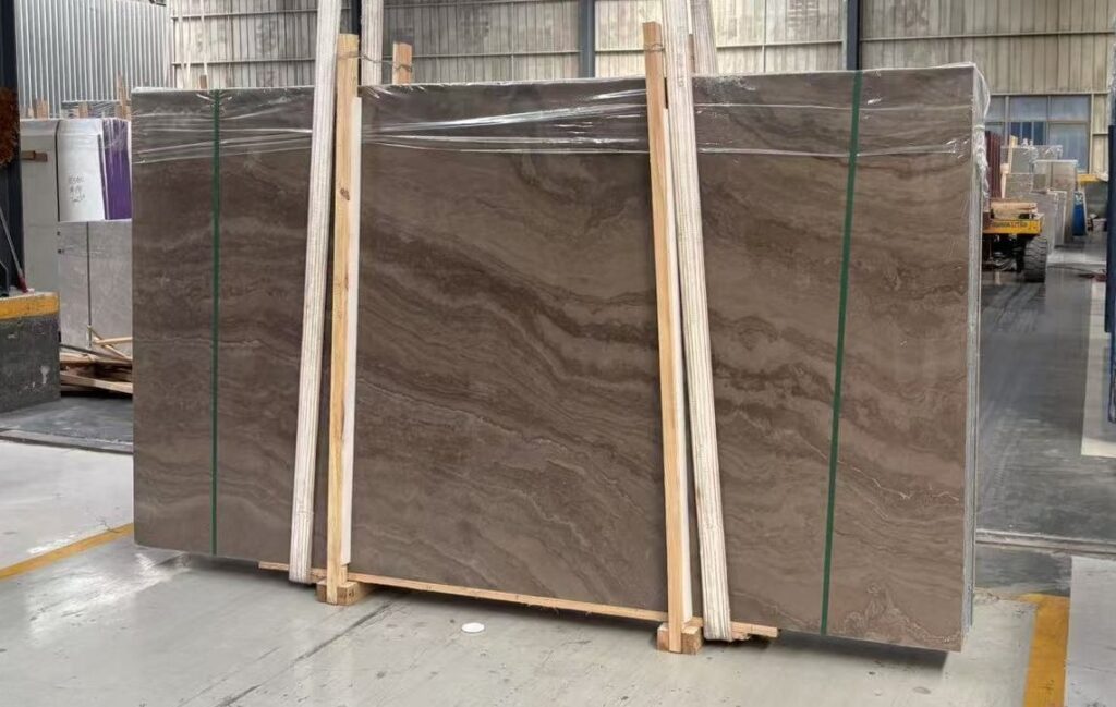 Three polished stone slabs standing in timber frames in an open workshop. The figure is wide and cloud-like rather than in close stripes: the veins have spread across the face, and the stone reads as a picture rather than as a wood grain.