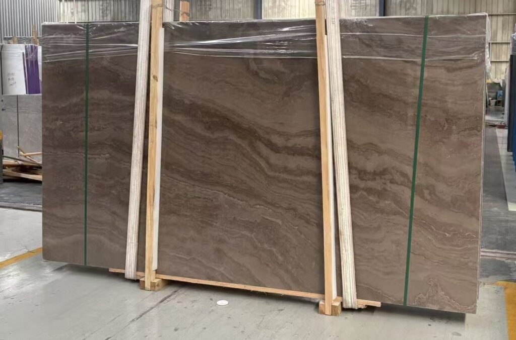 Three polished stone slabs standing in timber frames in a workshop. The figure is an open cloud-like pattern with the veining running in sweeping curves across the widest board.