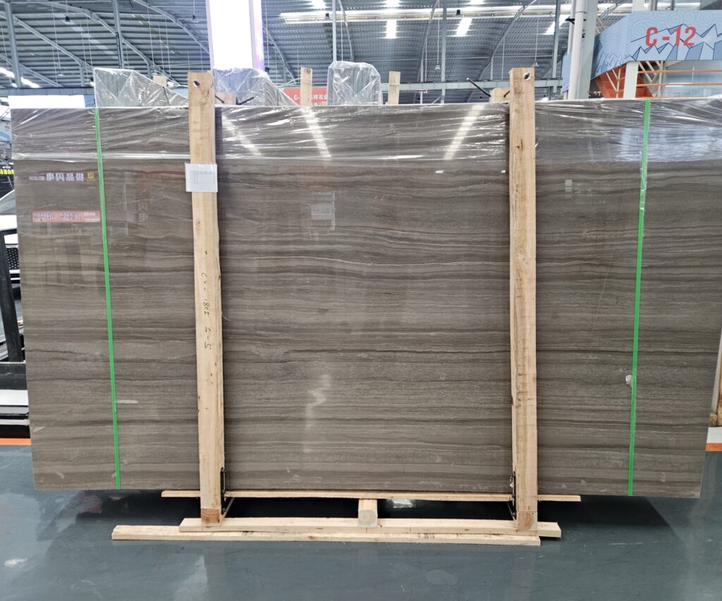 A large polished marble slab wrapped in film and strapped with green bands, standing upright on a wooden shipping frame