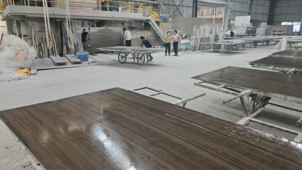 A wide workshop with polished marble slabs on trestles in the foreground and a gang saw with workers at the far end