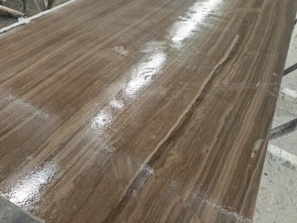 A close view of a wet polished marble slab showing straight dark brown veins running across a warm grey-brown base in even parallel lines