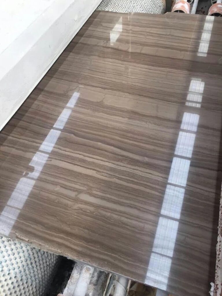 A polished marble slab lying flat with bright rectangular reflections of overhead lights on its glossy straight-grained surface
