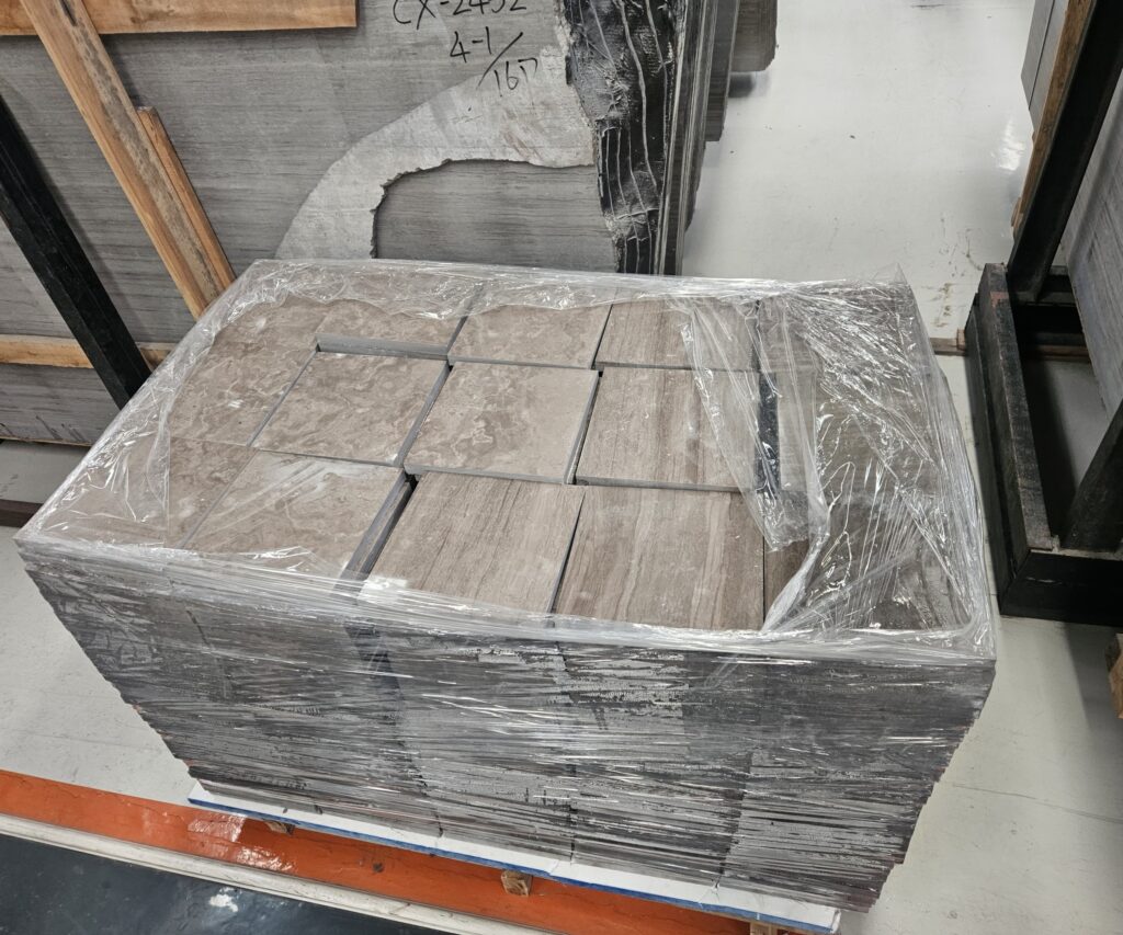 A shrink-wrapped stack of small rectangular cut stone pieces, in two tones of grey-brown, sitting on a workshop bench